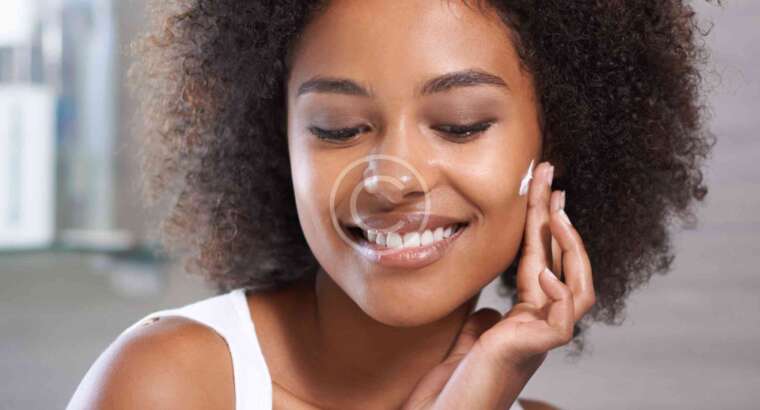 Smiling person applying skincare on face.