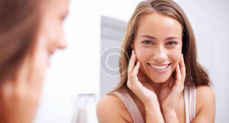 Smiling woman touching her face in mirror.