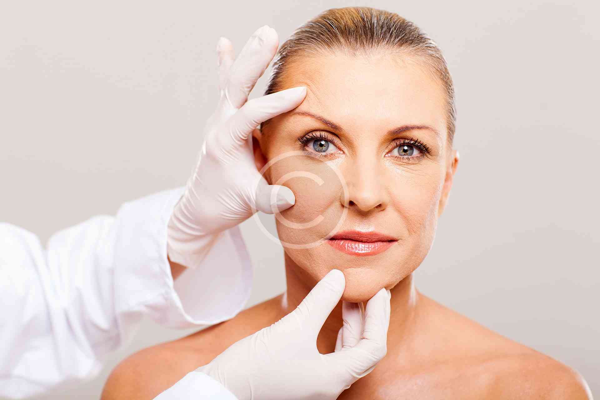 Woman receiving skin treatment with gloved hands.